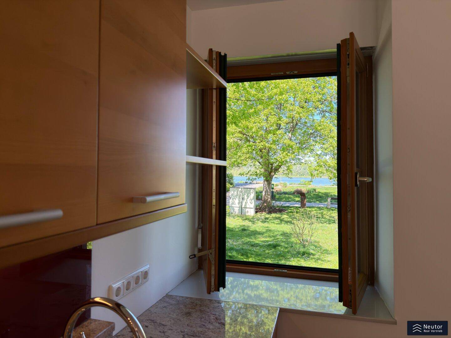 Küchenfenster mit Blick auf den See und grüne Uferlandschaft, bietet viel Tageslicht.