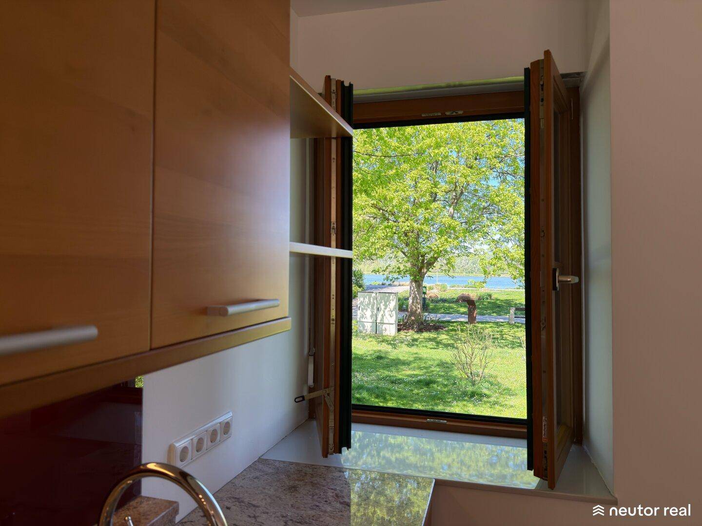 Küchenfenster mit Blick auf einen Baum und den See, das viel Tageslicht hereinlässt, sehr idyllisch.