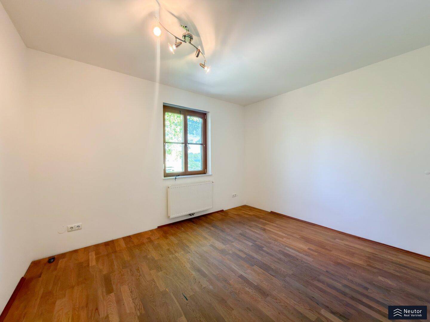 Helles Zimmer mit Holzboden und Fenster, bietet vielseitige Nutzungsmöglichkeiten.