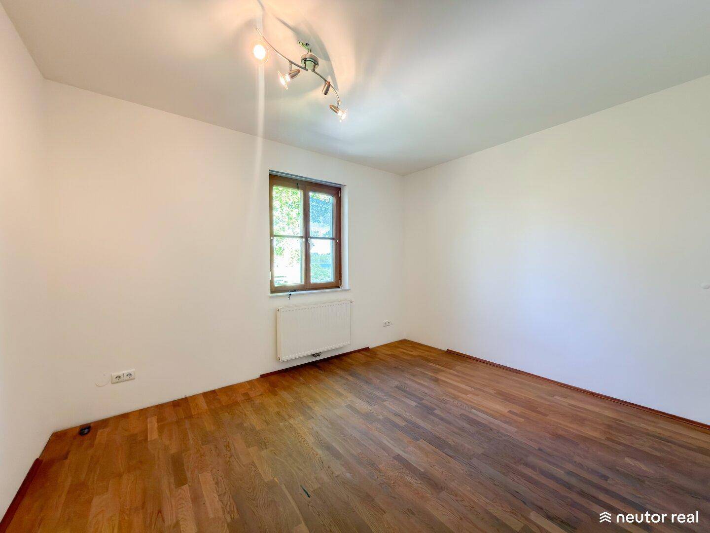 Helles Schlafzimmer mit Parkettboden, Fenster und Heizkörper unter dem Fenster, gemütlich und ruhig.