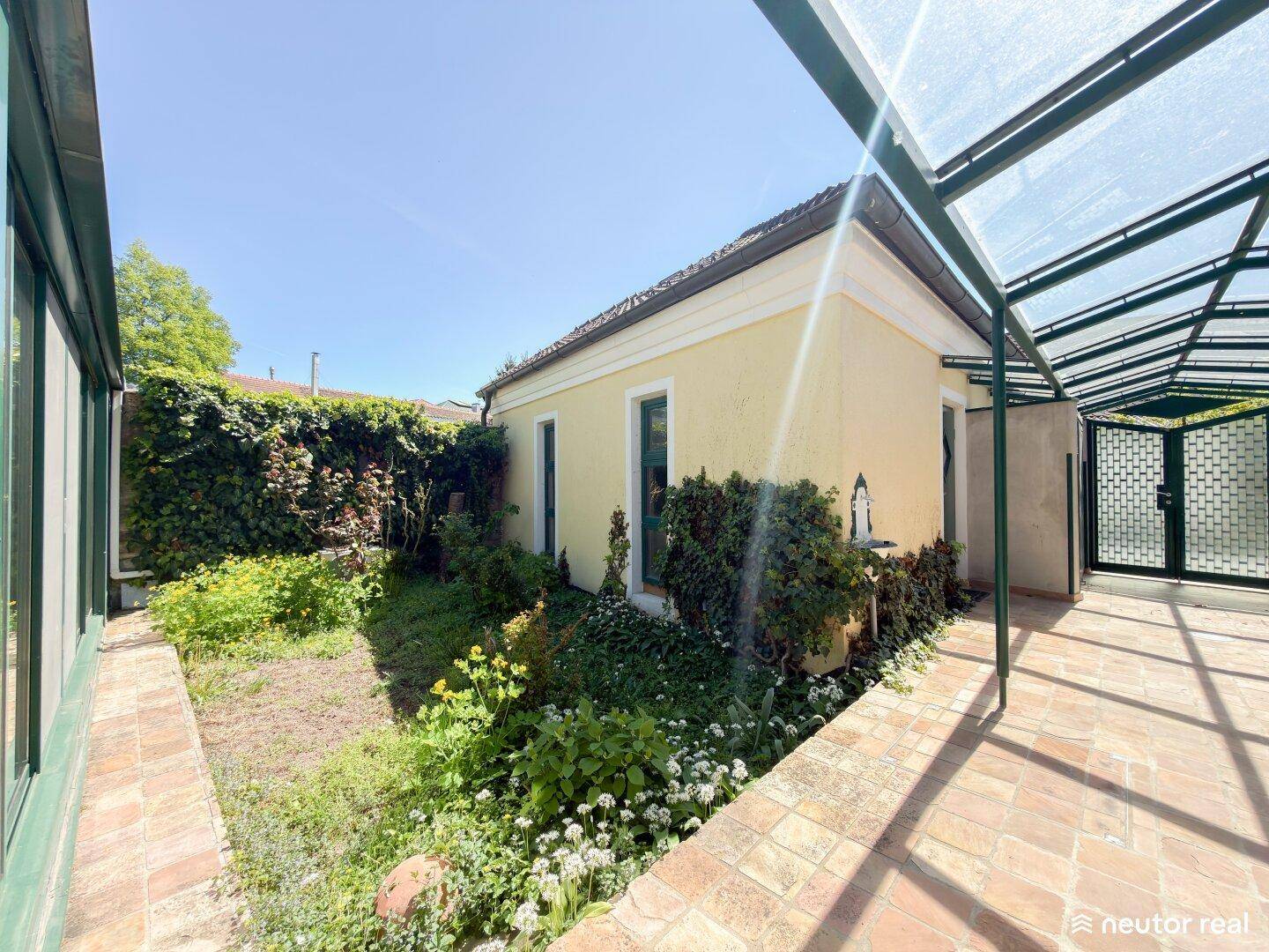 Gepflegter Gartenbereich neben dem Haus mit einer überdachten Pergola und viel Grün.