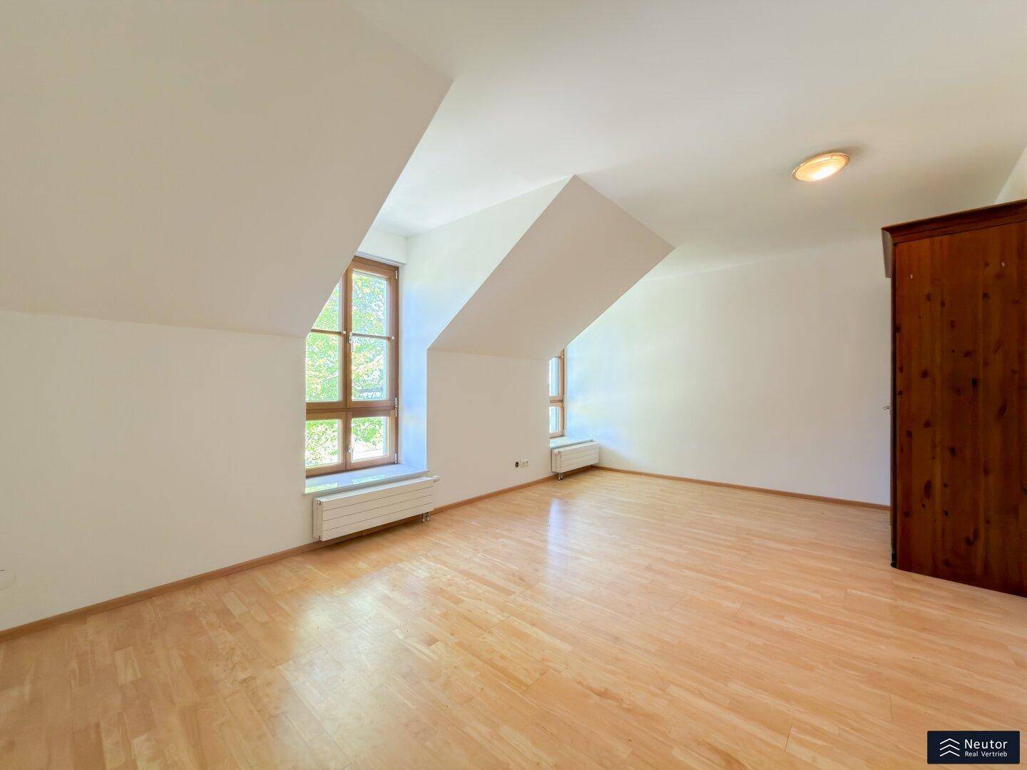 Helles Zimmer im Dachgeschoss mit Holzboden und schrägen Wänden, bietet gemütliche Atmosphäre.