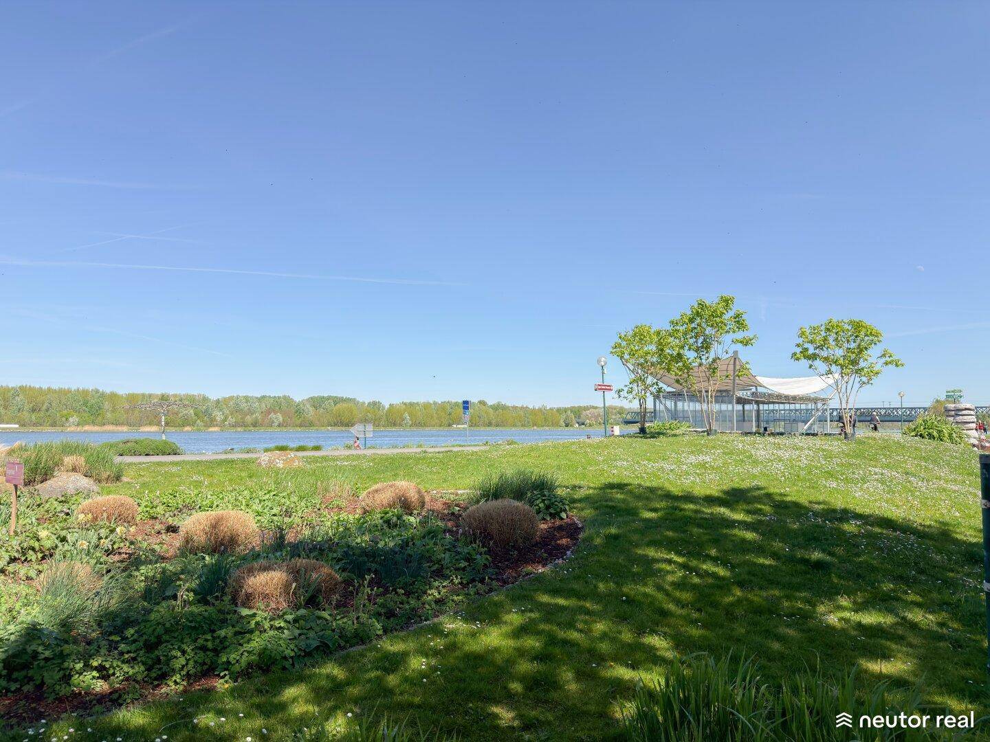 Grüne Parklandschaft mit Blick auf das Wasser und blühenden Pflanzen im Vordergrund.