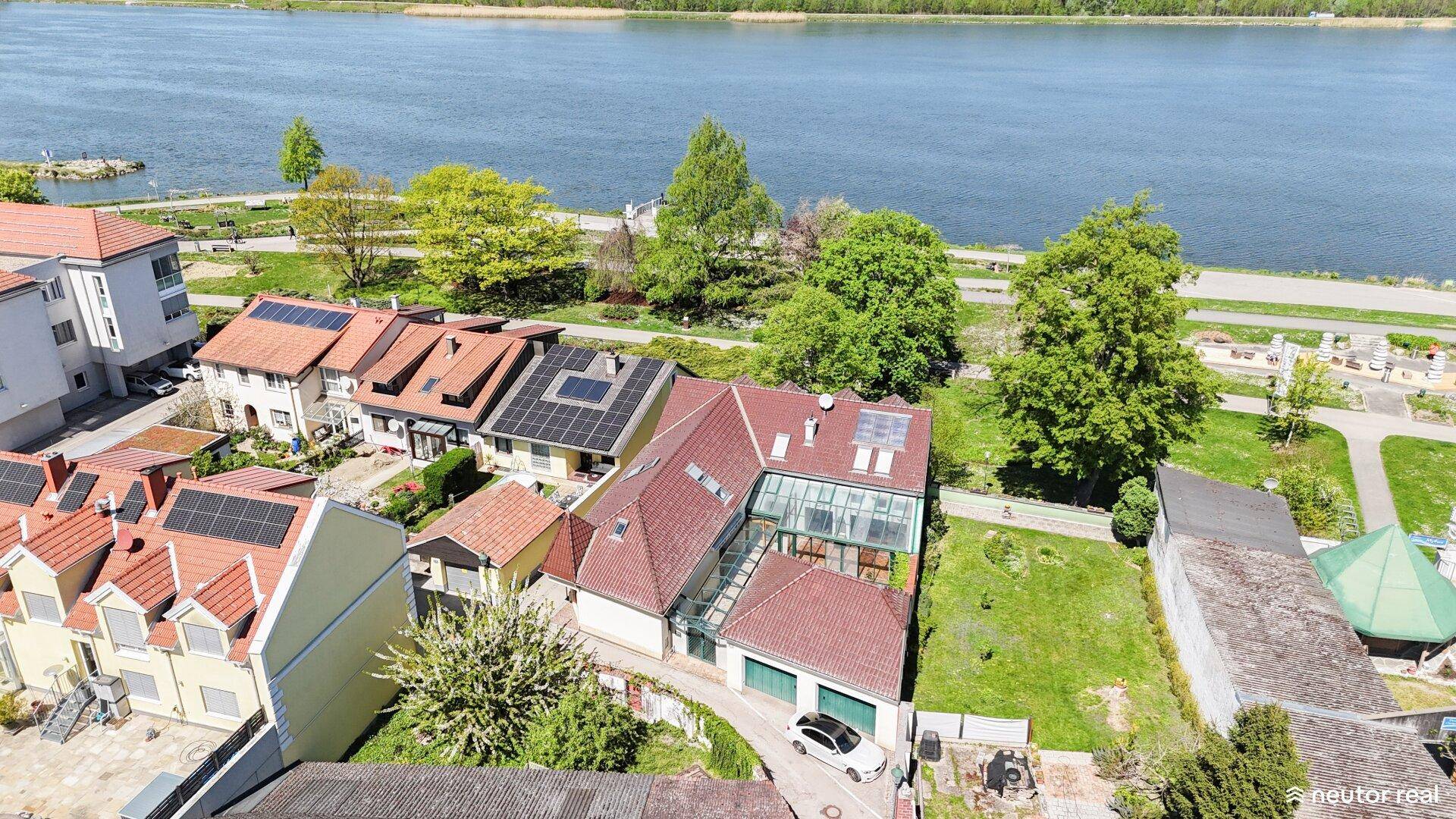 Luftaufnahme eines Wohngebiets am See mit Häusern und Solaranlagen auf den Dächern, idyllische Lage.