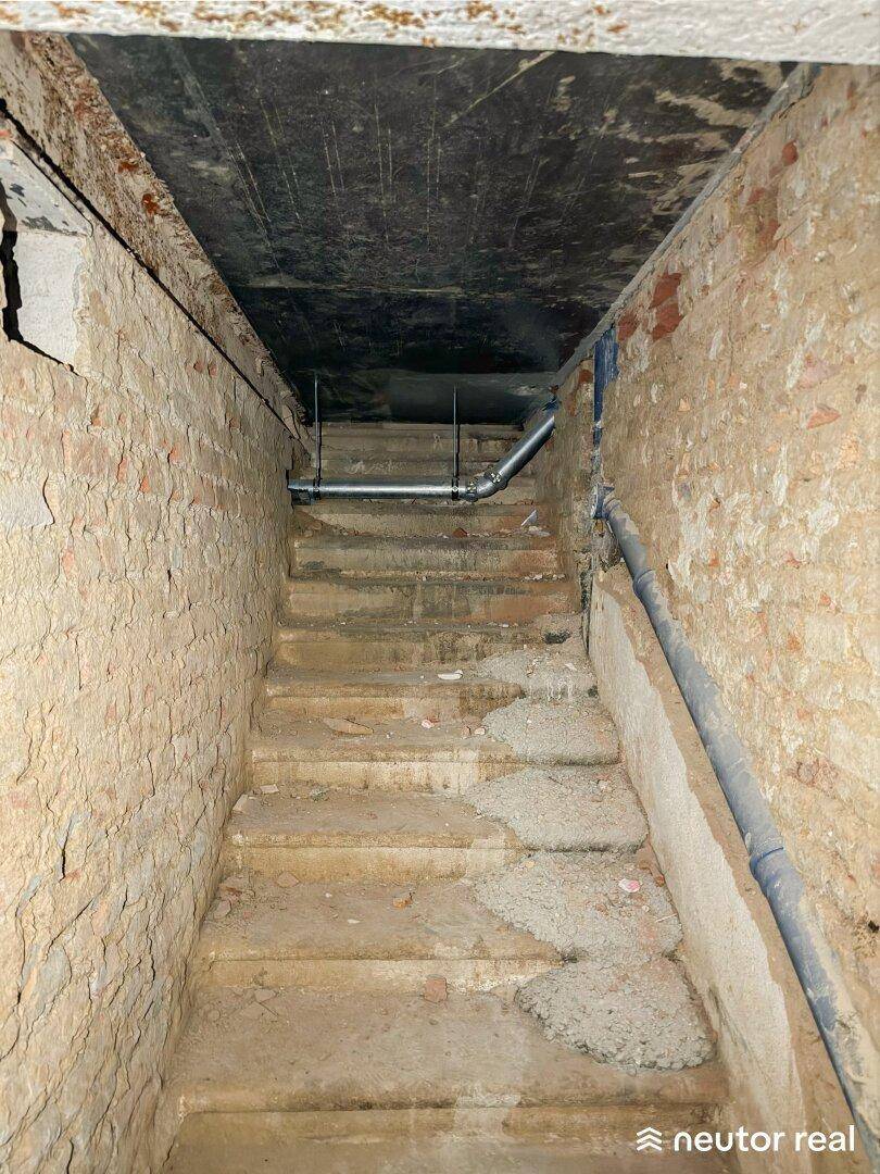 Steile Kellertreppe mit unverputzten Ziegelwänden und sichtbaren Rohren, die in den unteren Bereich führt.