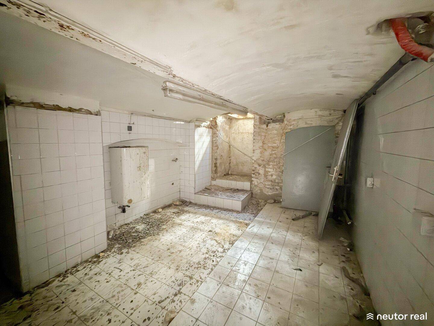 Kellerraum mit Boiler und Fliesenboden, der deutliche Spuren der Zeit zeigt und renovierungsbedürftig ist.