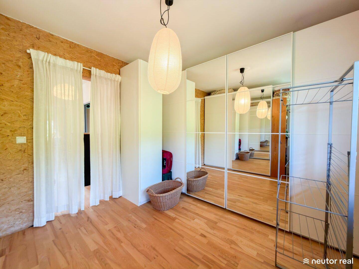 Helles Zimmer mit Spiegelschränken, Holzboden und viel Stauraum.