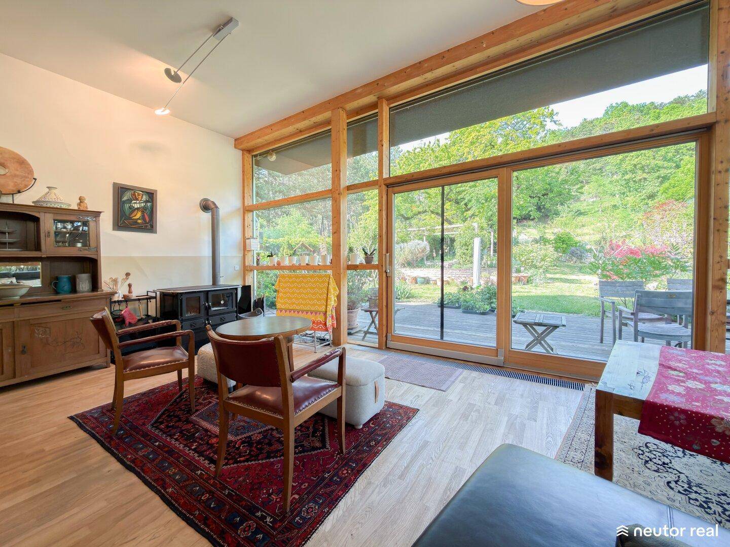 Gemütliches Wohnzimmer mit Holzboden, Kaminofen und großen Fenstern zum Garten.