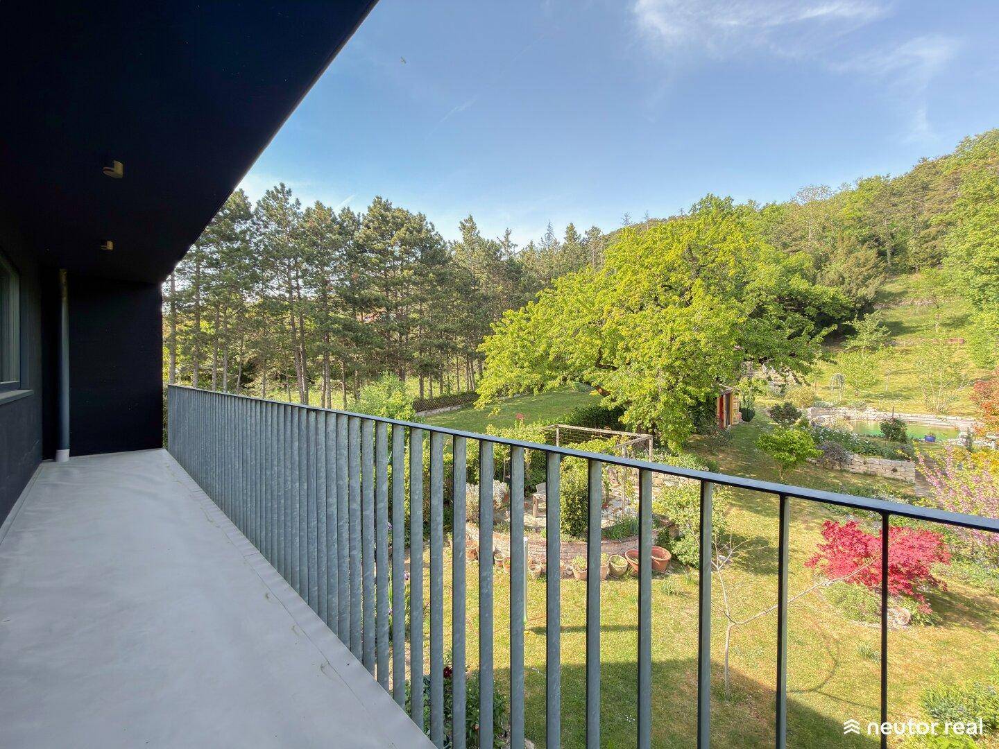 Langer Balkon mit Metallgeländer und weitem Blick über den Garten und die umliegenden Bäume.