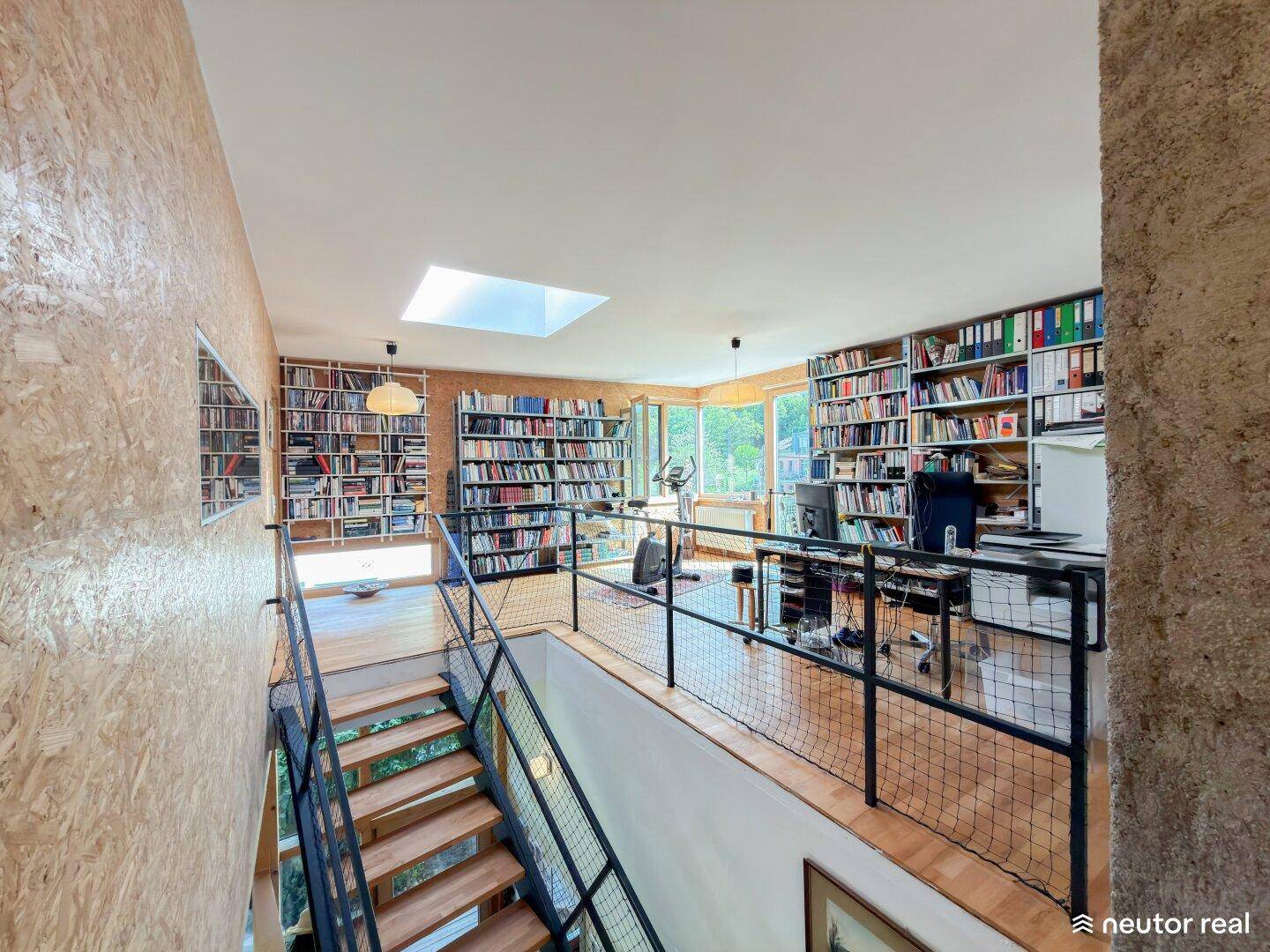 Helle Galerie mit Bücherregalen, Arbeitsbereich und Oberlicht, die einen offenen Raum schafft.