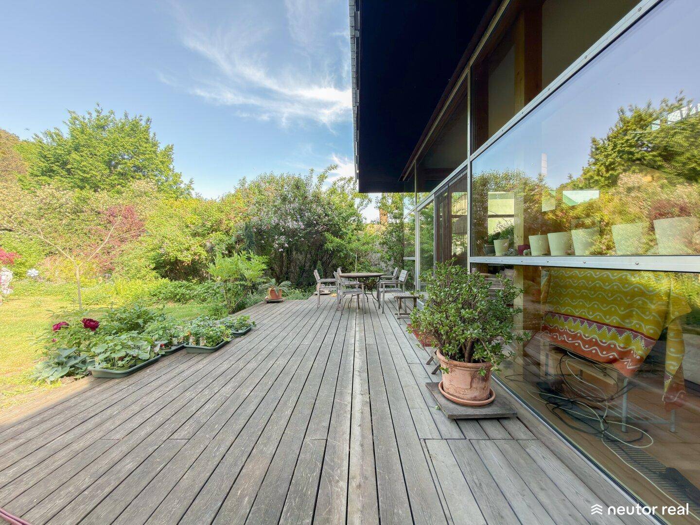 Große Holzterrasse mit Sitzgelegenheiten und direktem Zugang zum grünen Garten.