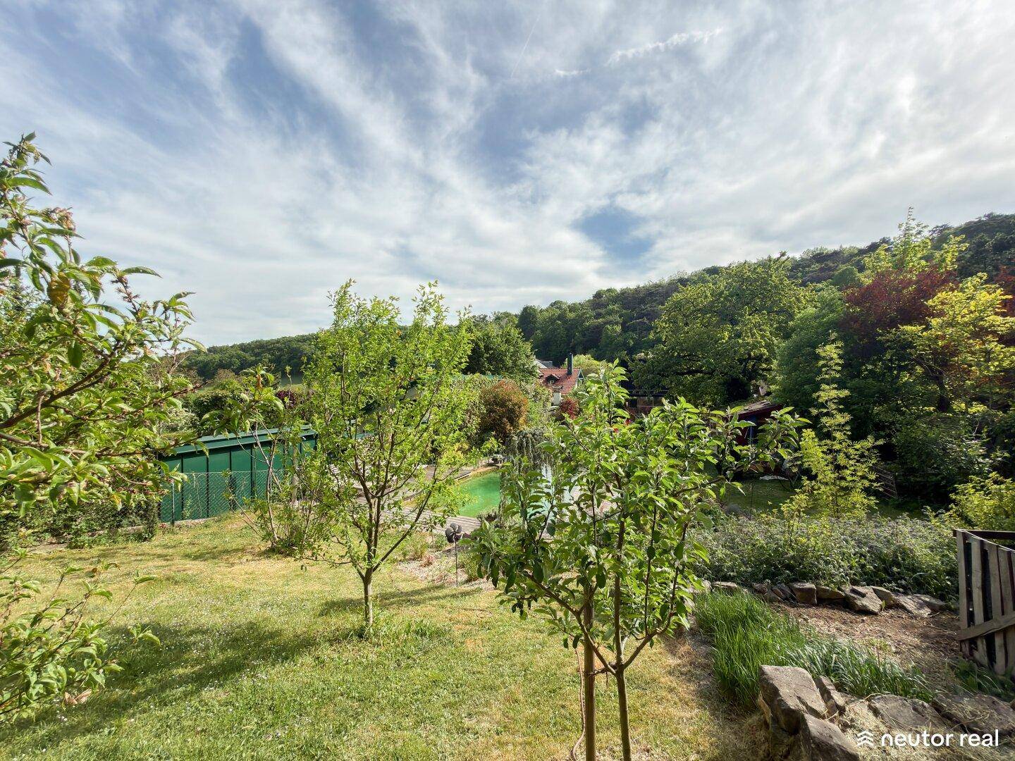 Weitläufiger Gartenbereich mit jungen Obstbäumen und einem weiten Blick in die grüne Landschaft unter Wolken.