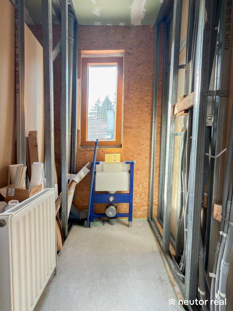 Unfertiger Raum, vorbereitet für ein WC, mit Fenster und sichtbaren Installationen.