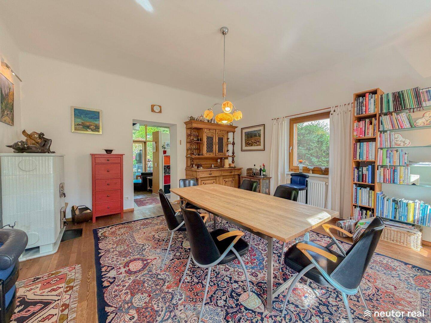 Geräumiges Esszimmer mit großem Holztisch, Bücherregalen und einem traditionellen Kachelofen.