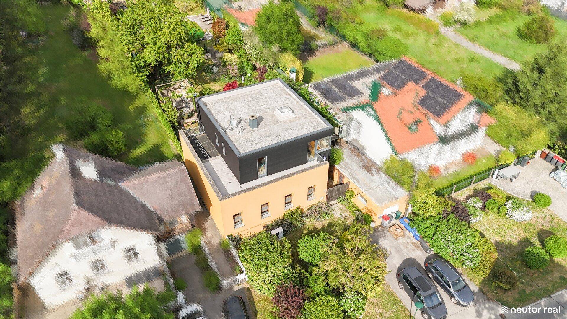 Luftaufnahme des modernen Hauses mit Flachdach und umliegenden Gebäuden in grüner, sonniger Umgebung.