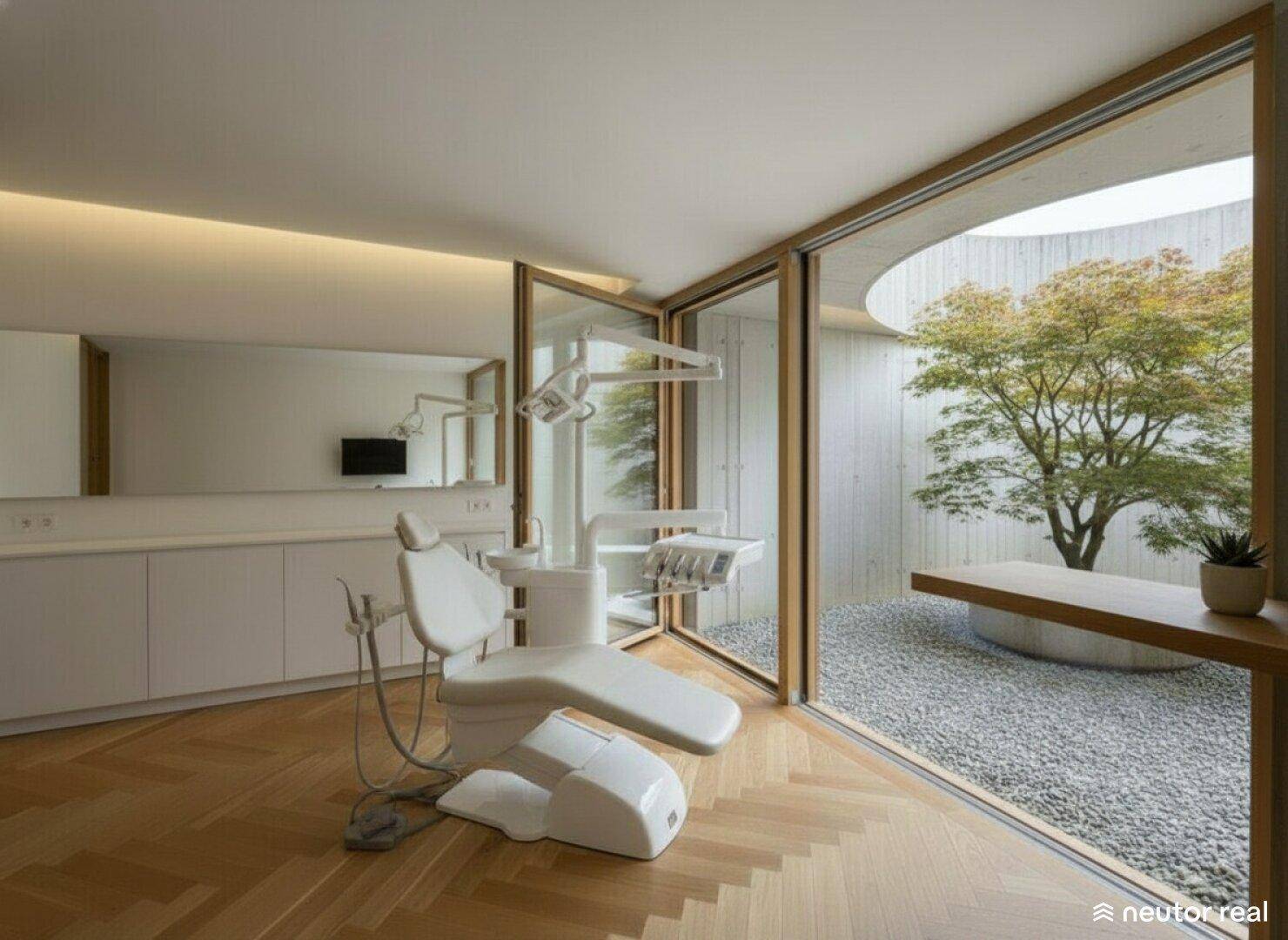 Behandlungszimmer mit medizinischem Stuhl, weißen Schränken und Blick auf einen ruhigen Innenhof.