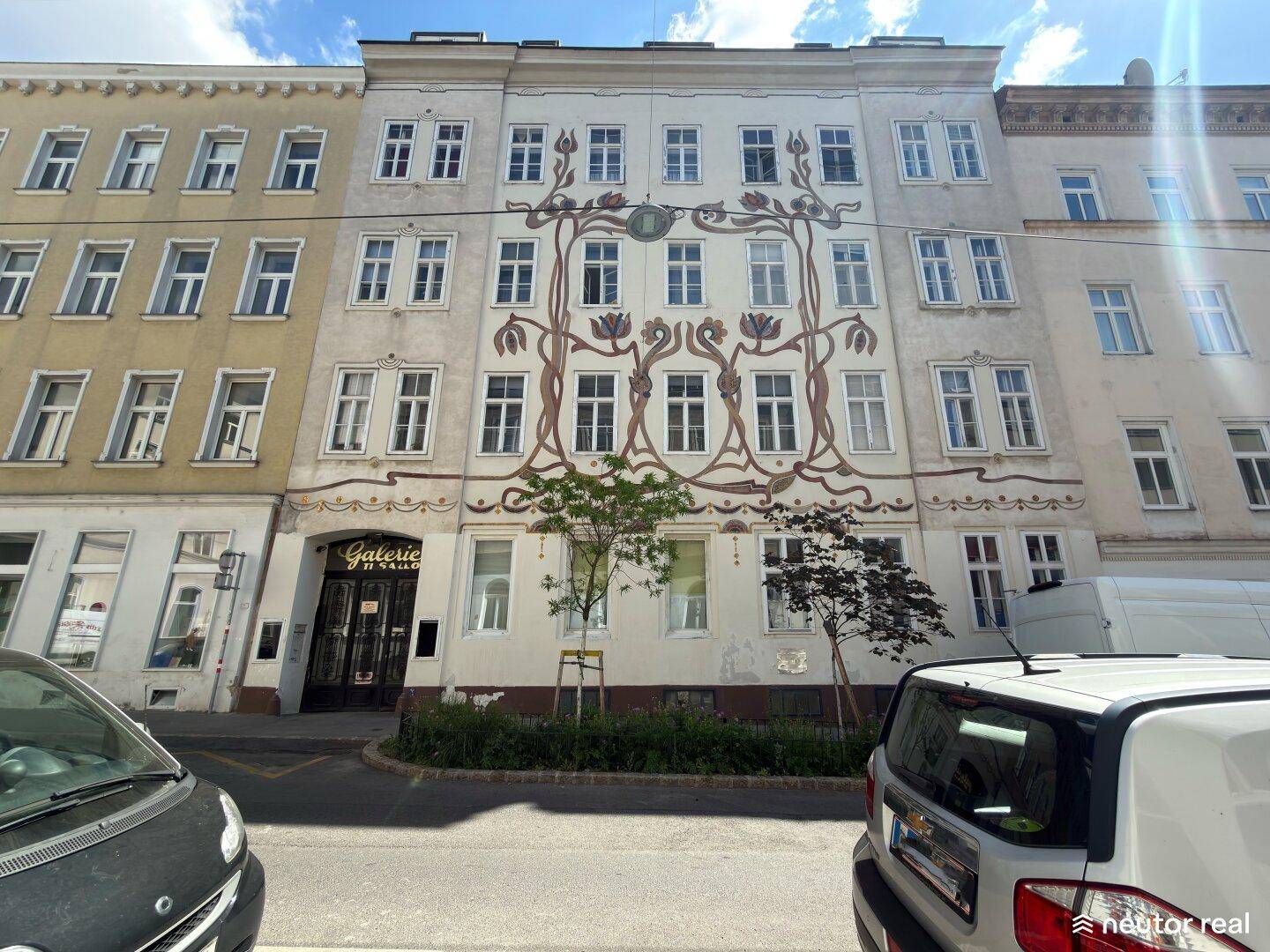 Historisches Gebäude mit kunstvoller Fassadenmalerei und parkenden Autos davor.