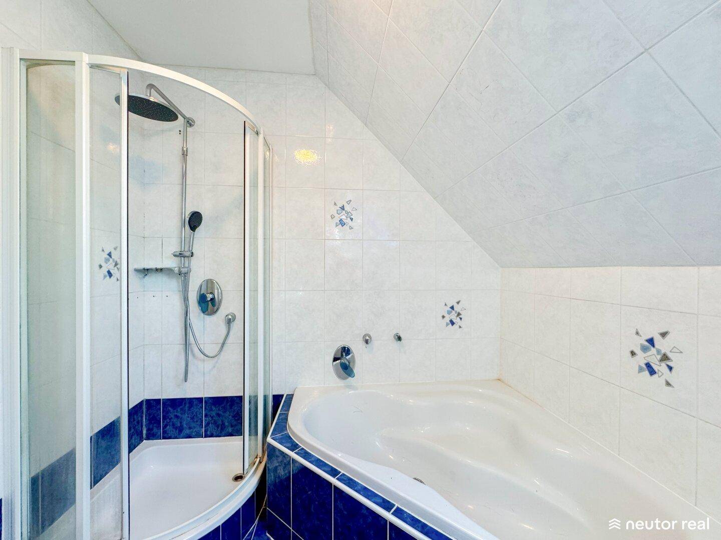 Badezimmer mit Badewanne, Duschkabine und blauen Akzentfliesen in hellem Ambiente.