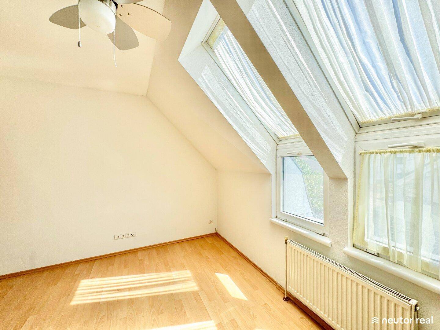 Helles Schlafzimmer mit Holzparkett, Dachfenstern und Deckenventilator für angenehmes Klima.