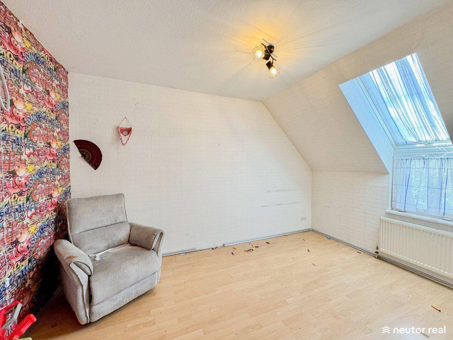 Dachzimmer mit weißer Ziegelwandoptik, Dachschräge und einem gemütlichen Sessel unter dem Dachfenster.