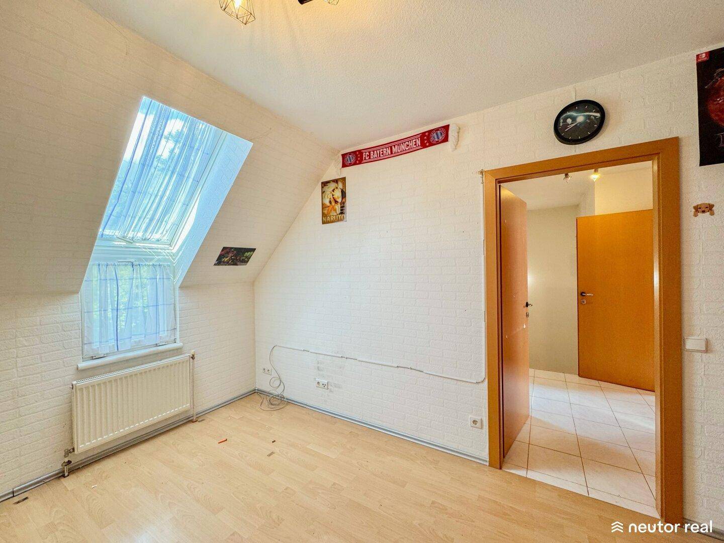 Helles Dachzimmer mit weißer Ziegelwandoptik, Dachschräge und einem großen Dachfenster.