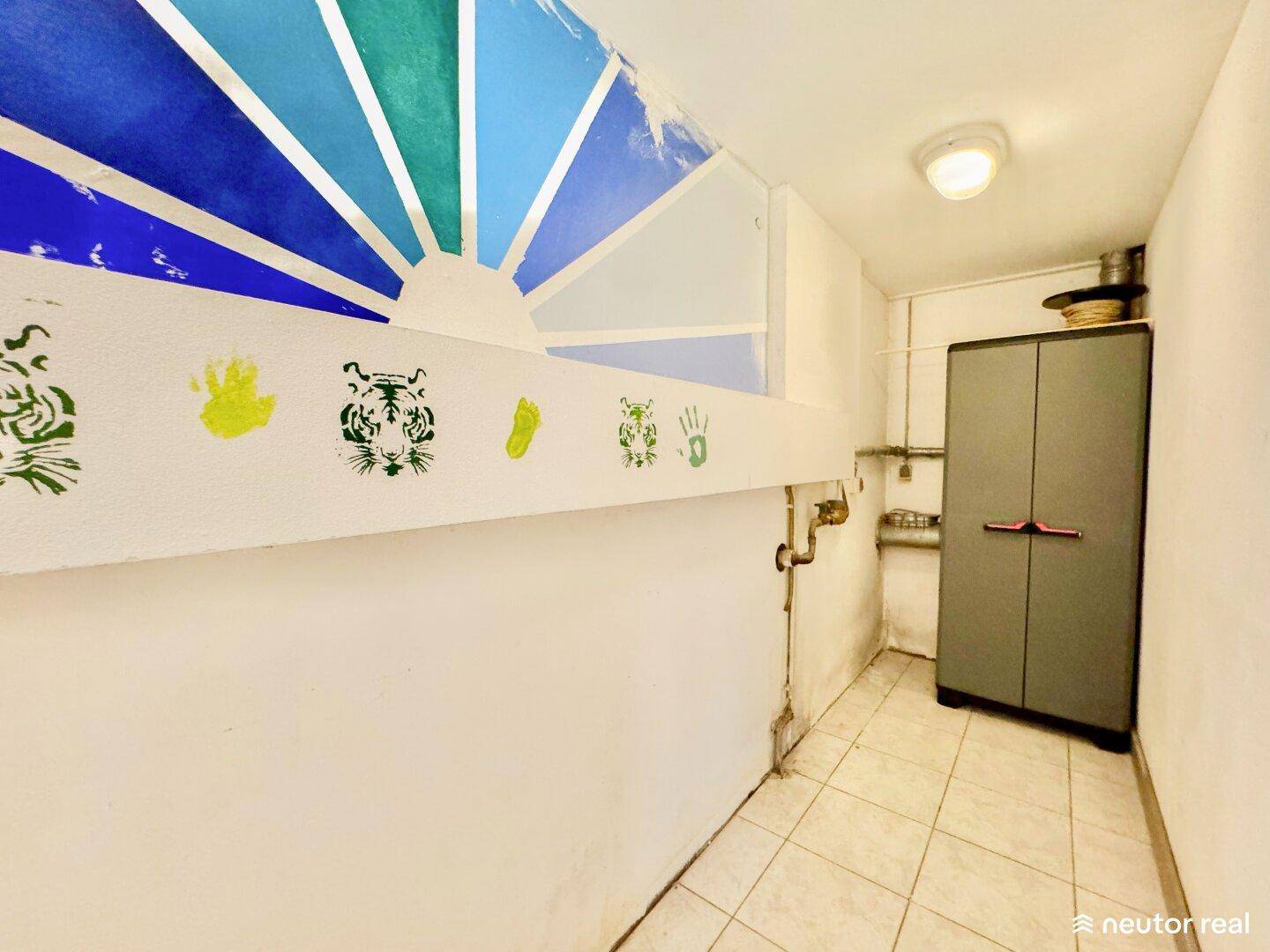 Kellerraum mit praktischem Schrank, sichtbaren Rohren und einer kreativ bemalten Wand.