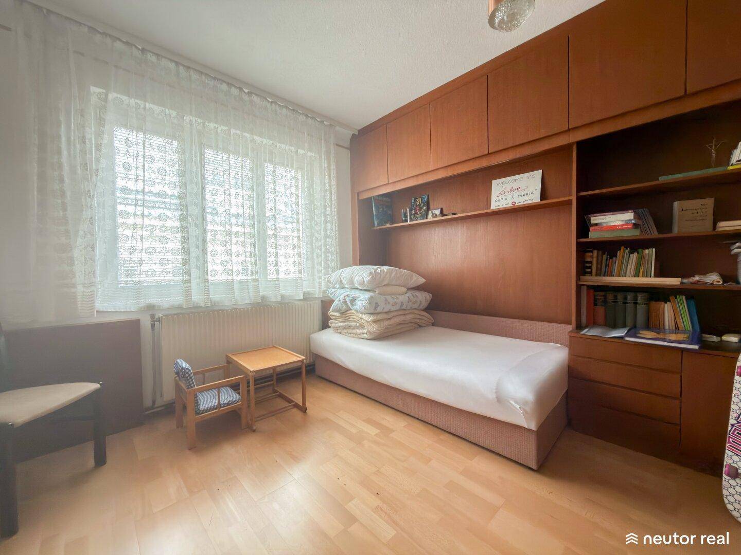 Schlafzimmer mit Holzboden, großem Fenster und integrierten Holzmöbeln.