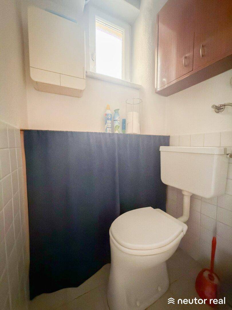Separate Toilette mit Fenster, weißen Fliesen und einfacher Ausstattung.