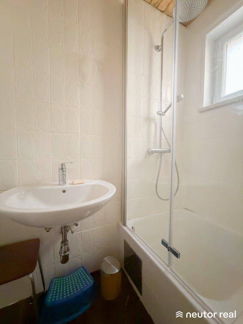 Badezimmer mit Dusche, Waschbecken und Fenster für Belüftung.