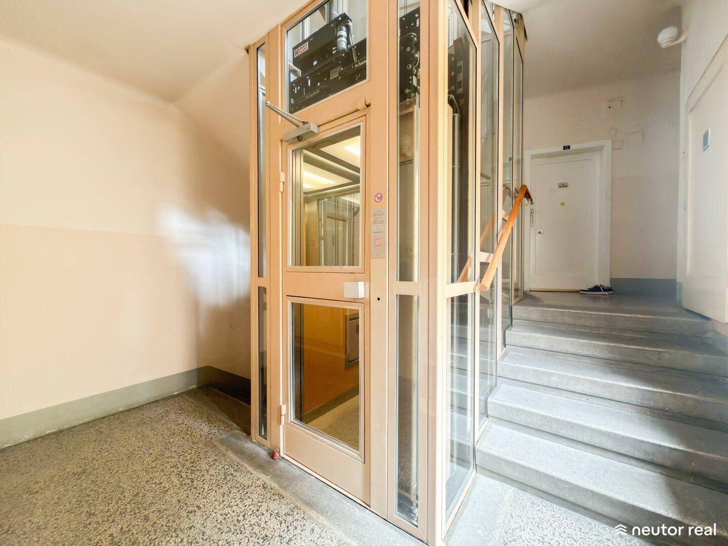 Moderner Glasaufzug im Treppenhaus eines Mehrfamilienhauses.