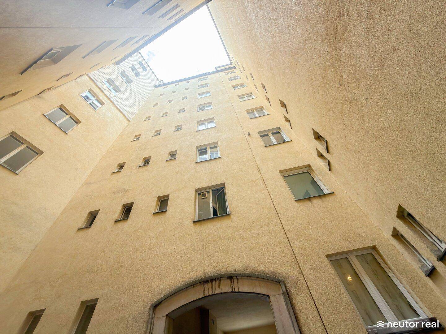 Innenhof eines Wohngebäudes mit hohen Wänden und Blick zum Himmel.