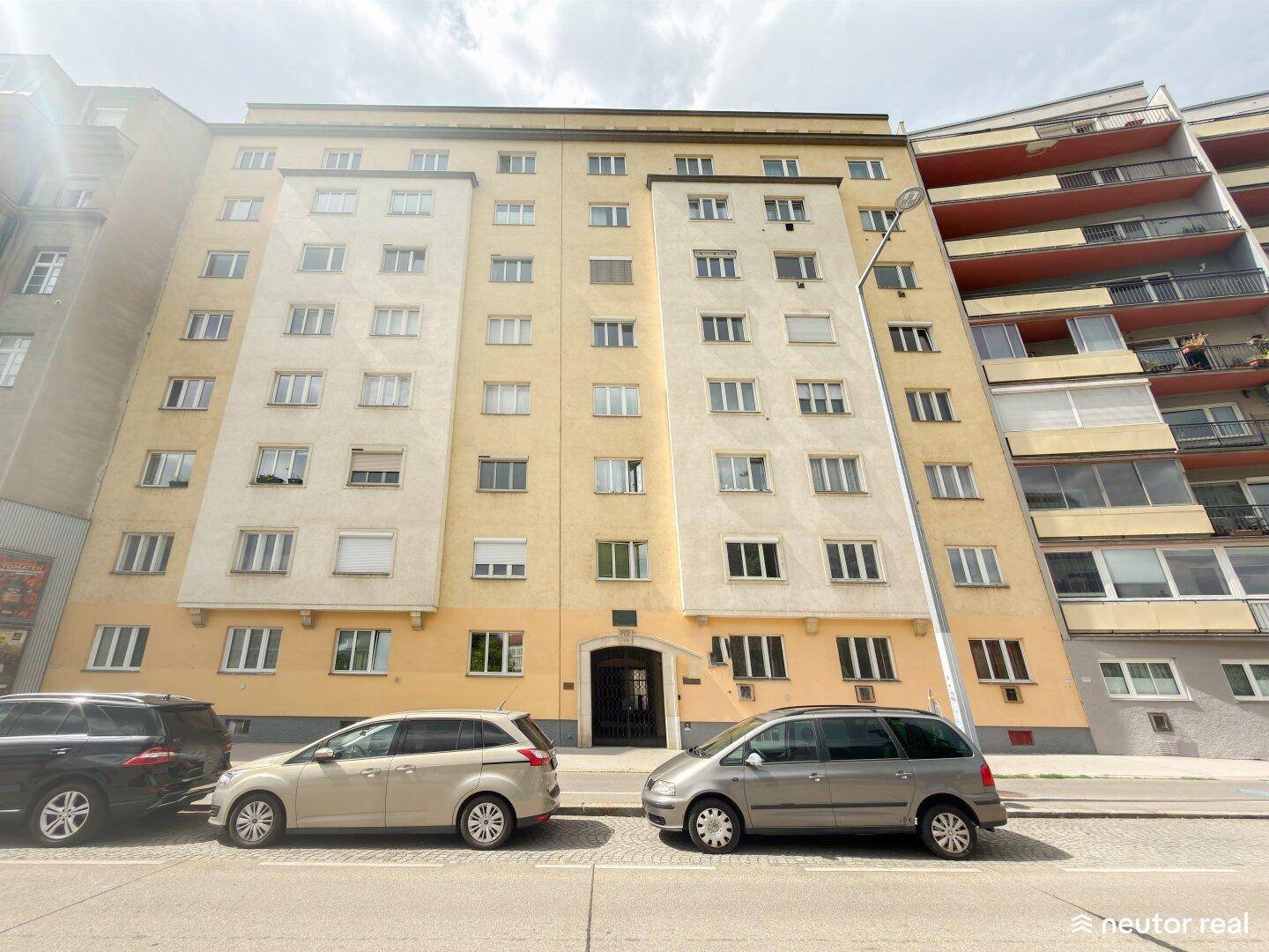 Fassade eines Mehrfamilienhauses mit vielen Fenstern und parkenden Autos.