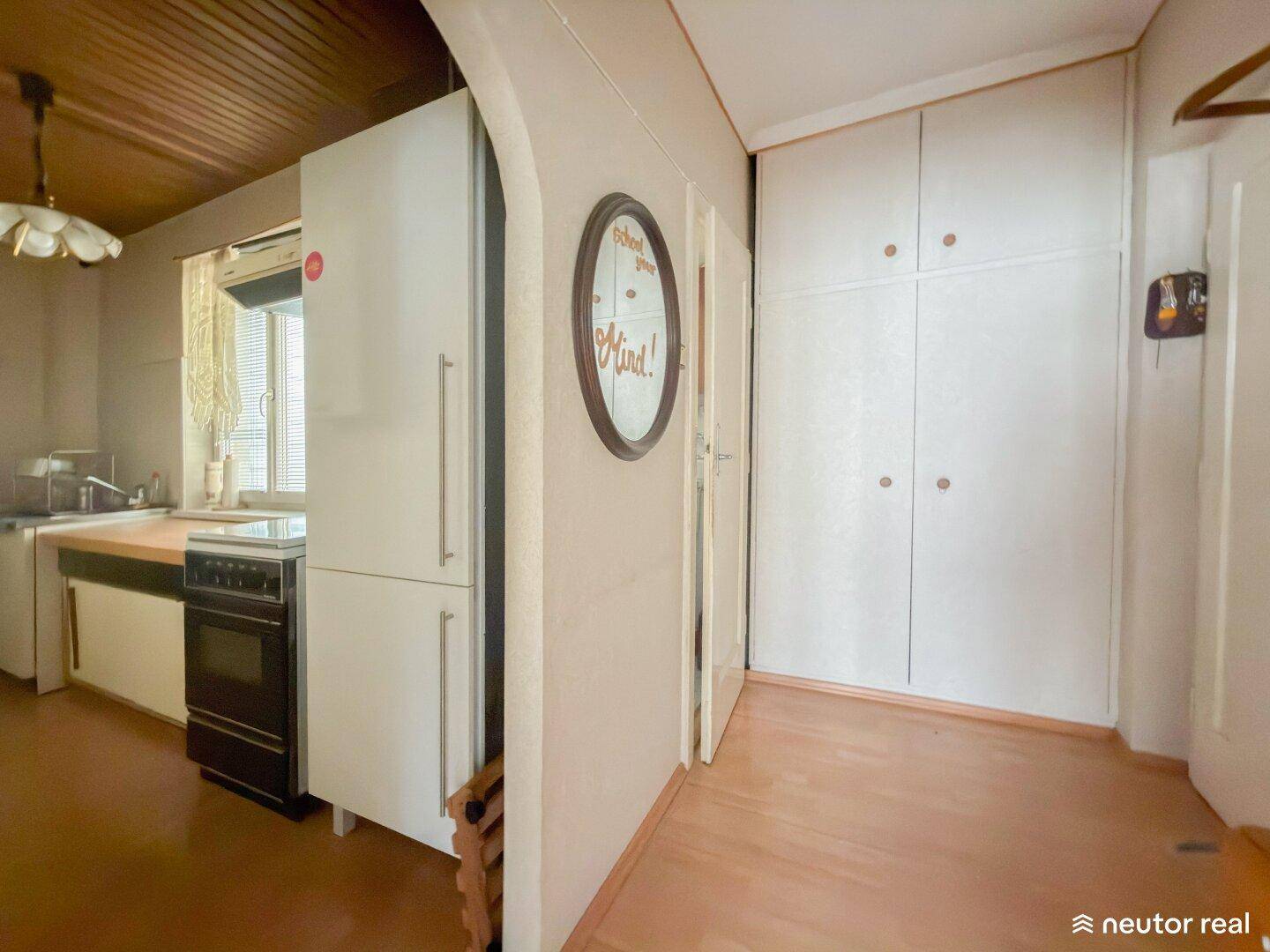 Schmale Küche mit Holzdecke, Einbauschränken und Zugang zum Flur.