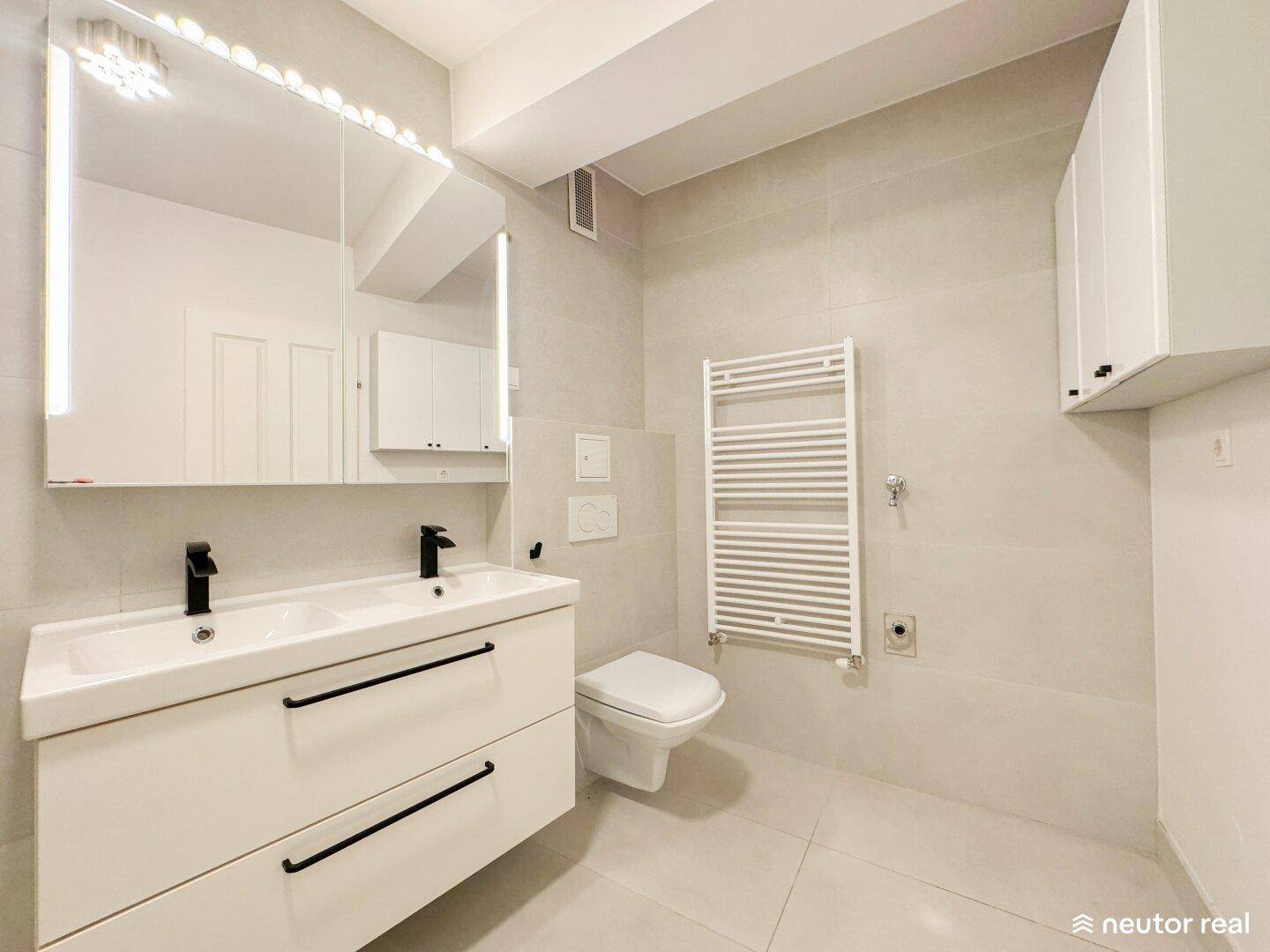Elegantes Badezimmer mit Doppelwaschbecken, wandhängender Toilette und beheiztem Handtuchhalter.