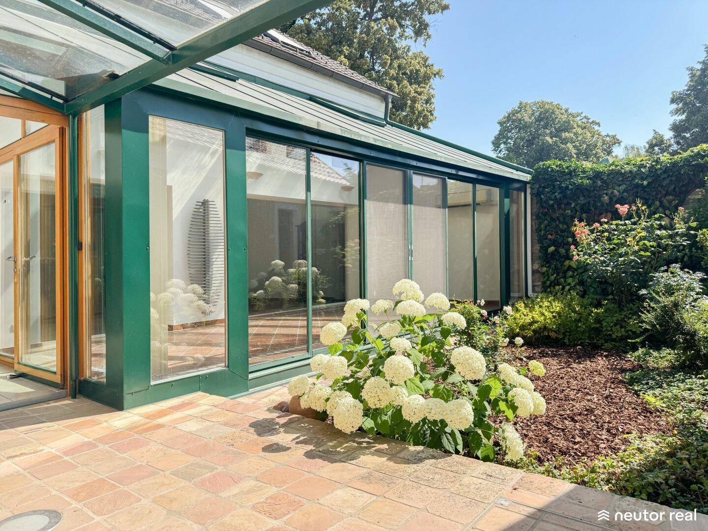 Sonniger Gartenbereich mit blühenden Hortensien und einer angrenzenden Terrasse, perfekt für den Sommer.