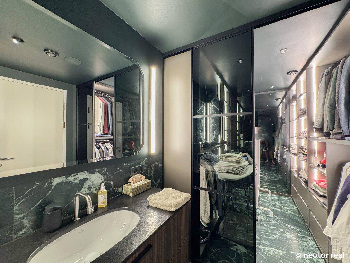 Modernes Badezimmer mit dunklen Marmorfliesen und integriertem Waschbecken, angrenzend an einen begehbaren Kleiderschrank.