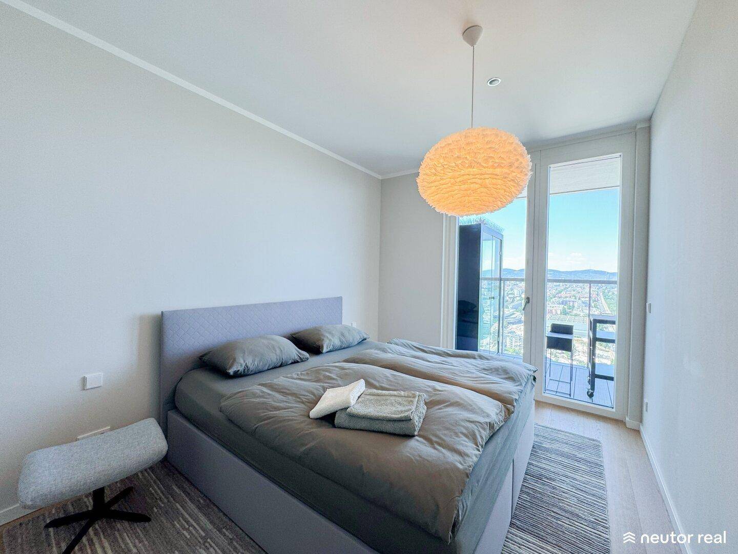 Helles Schlafzimmer mit Doppelbett und Zugang zu einem Balkon mit Panoramablick.
