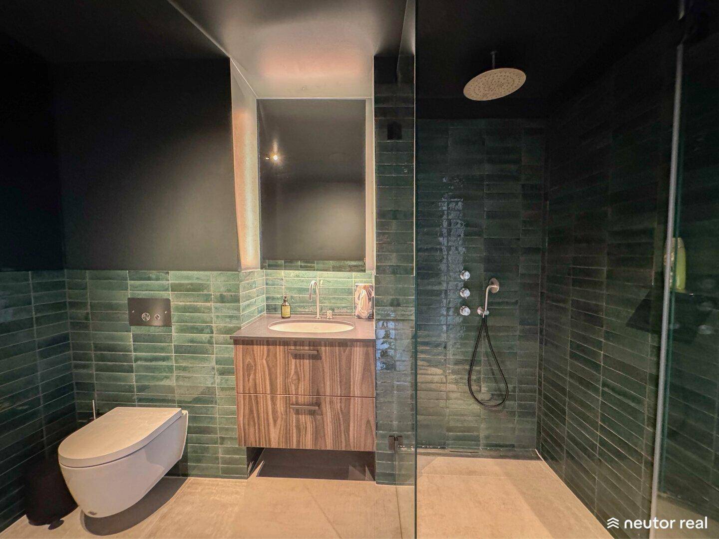 Modernes Badezimmer mit grünen Fliesen, wandhängendem WC und großer begehbarer Dusche.