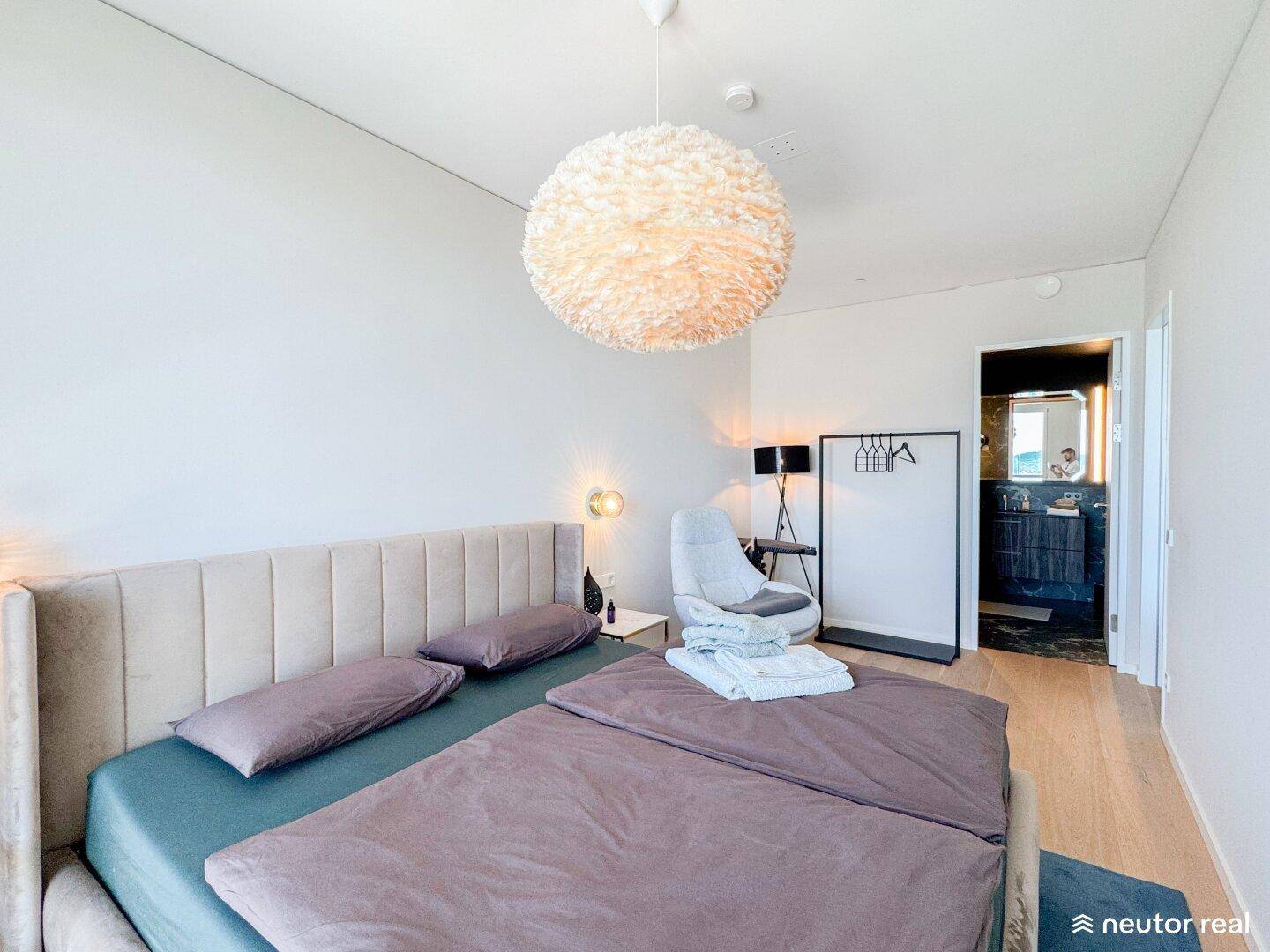 Helles Schlafzimmer mit Doppelbett und direktem Zugang zu einem modernen Badezimmer.