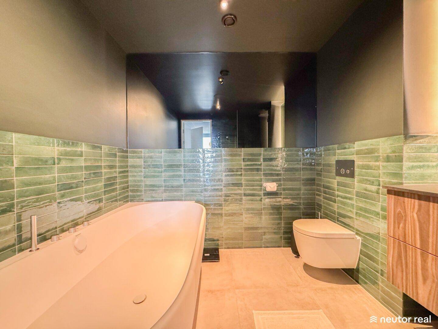 Modernes Badezimmer mit Badewanne, wandhängendem WC und grünen Wandfliesen.
