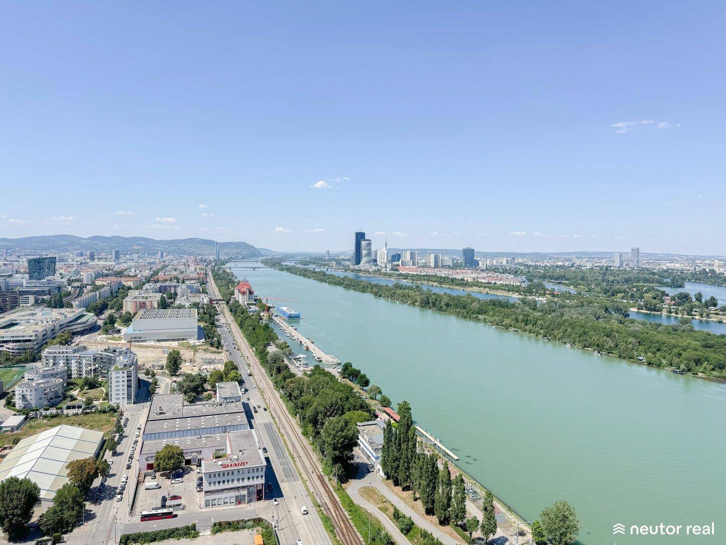 Panoramablick auf die Stadt Wien mit der Donau und umliegenden Grünflächen unter blauem Himmel.