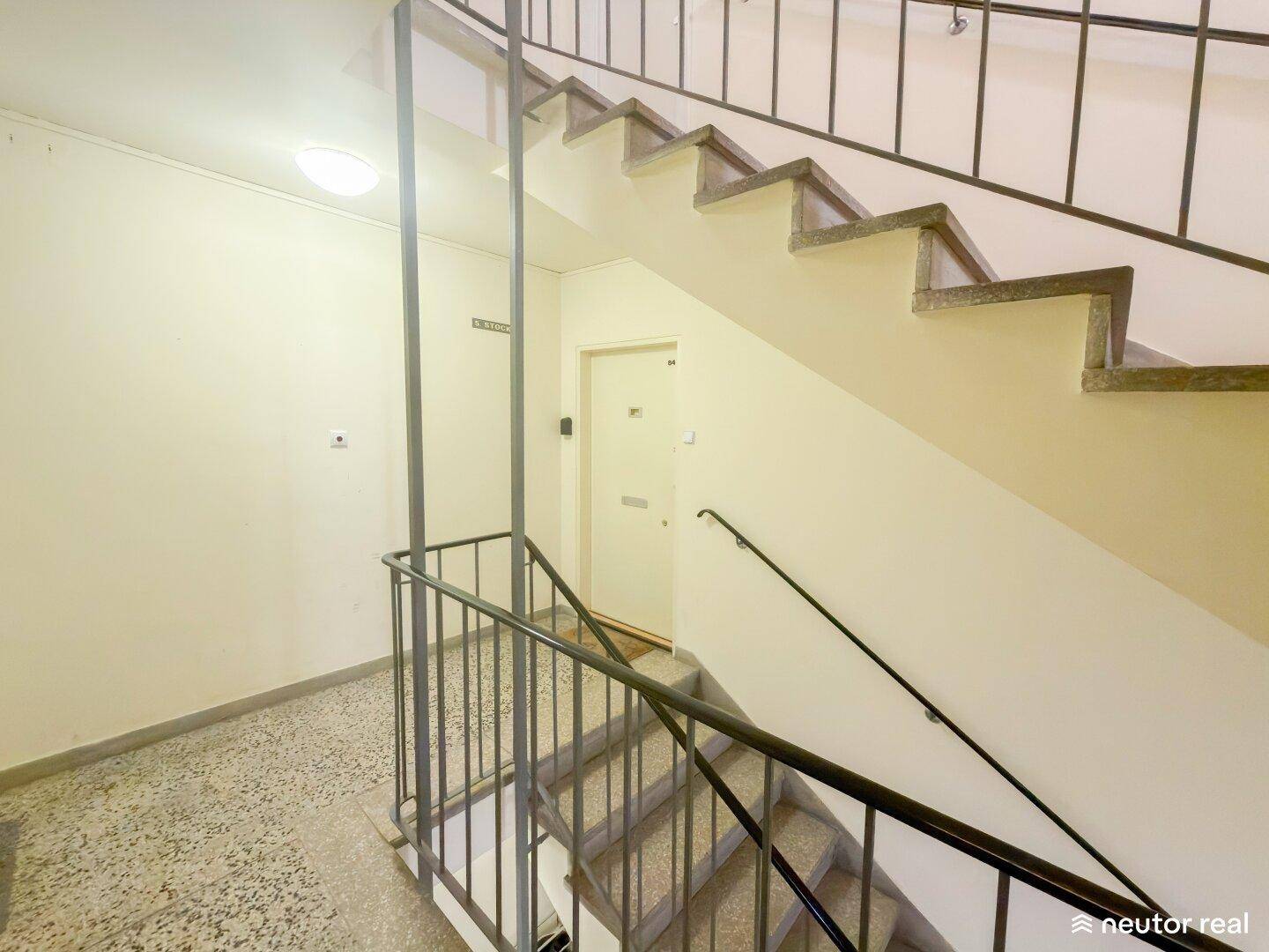 Treppenhaus mit Steinstufen und Metallgeländer in einem Mehrfamilienhaus.