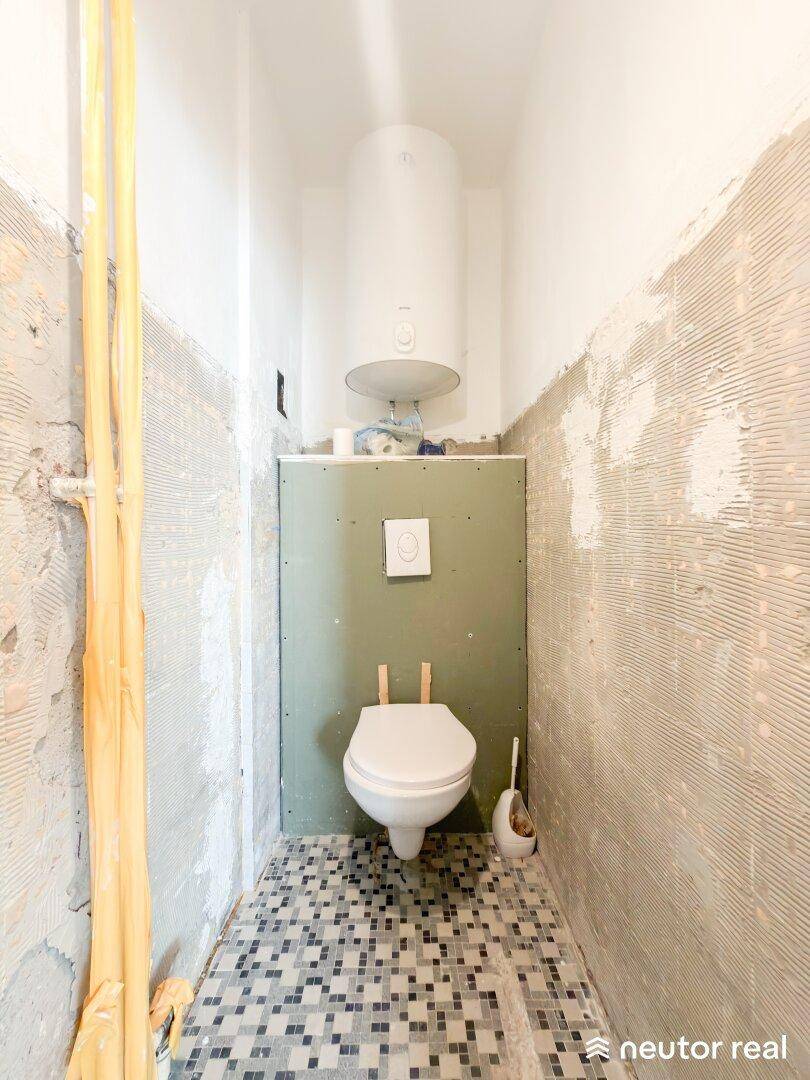Unfertiges WC mit Wand-WC und kleinem Mosaikfliesenboden, bereit zur Fertigstellung.
