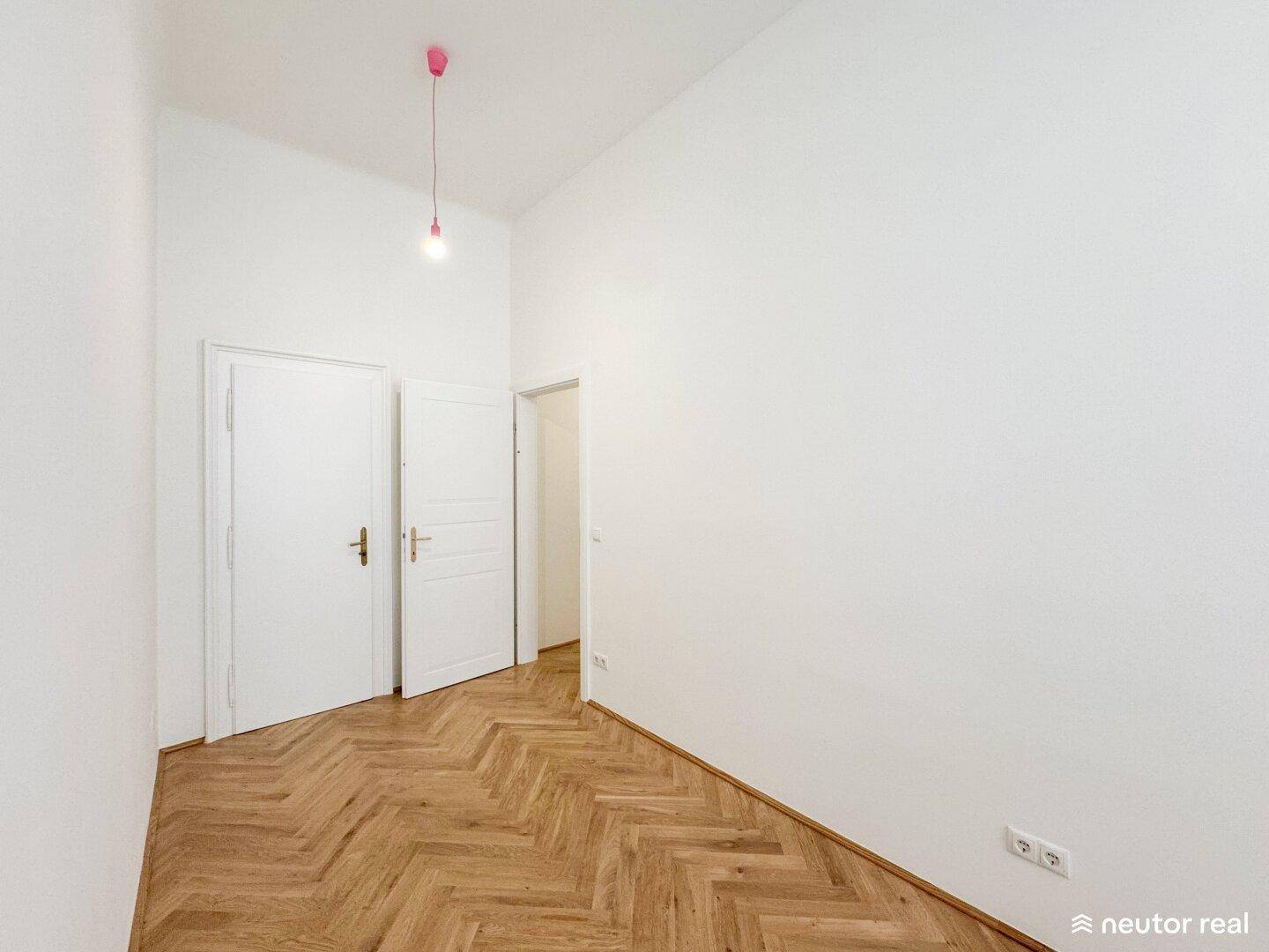 Leeres Zimmer mit Fischgrätparkett und zwei weißen Türen, bereit zur Einrichtung.