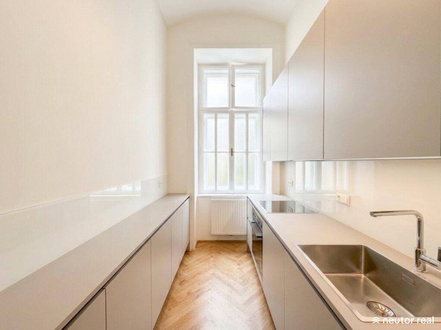 Schmale, moderne Küche mit hellgrauen Schränken, integriertem Kochfeld und Fenster.