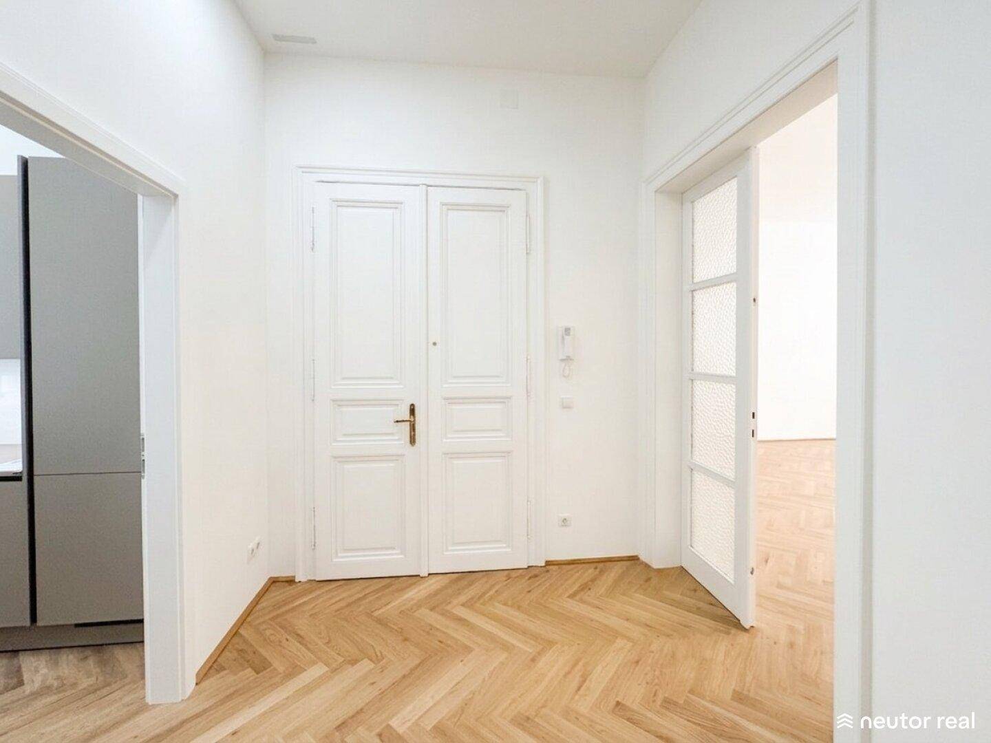 Heller Flur mit Fischgrätparkett, weißen Türen und Zugang zu Küche und weiteren Zimmern.