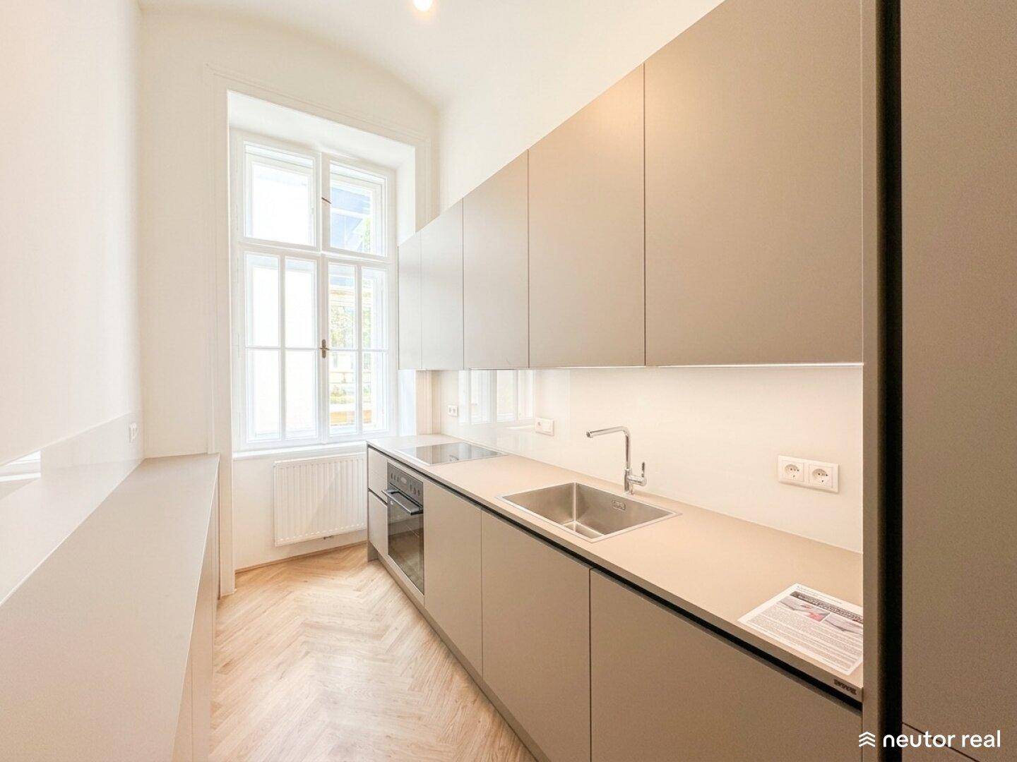 Moderne Küche mit hellgrauen Schränken, Spüle, Kochfeld und Fenster für natürliches Licht.