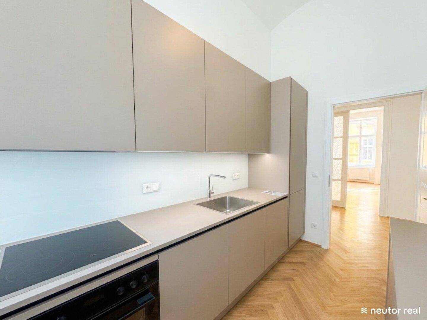 Gut ausgestattete, moderne Küche mit hellgrauen Schränken, Kochfeld und Blick in den Flur.