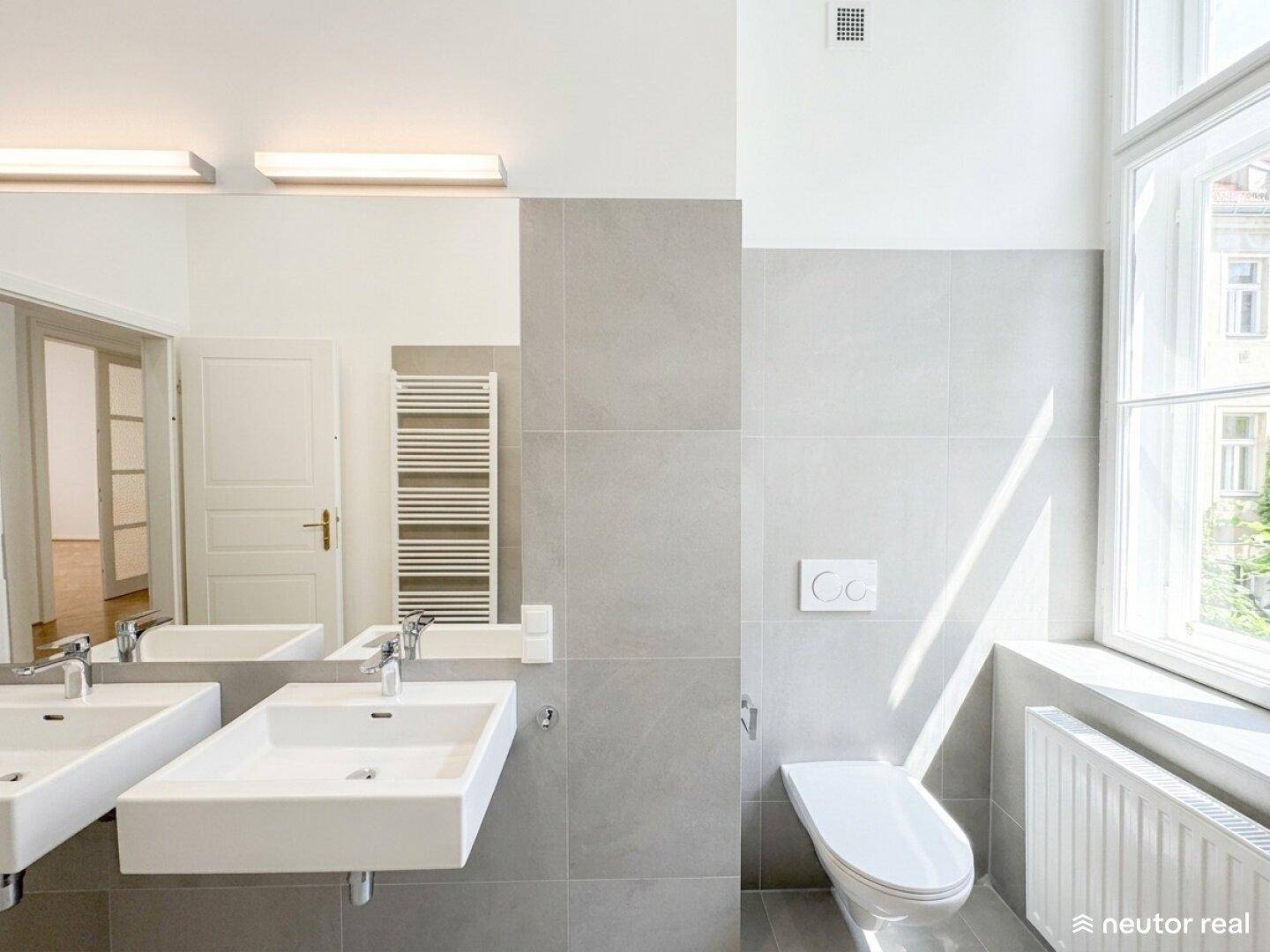 Modernes Badezimmer mit Doppelwaschbecken, Wand-WC und großem Fenster für Tageslicht.