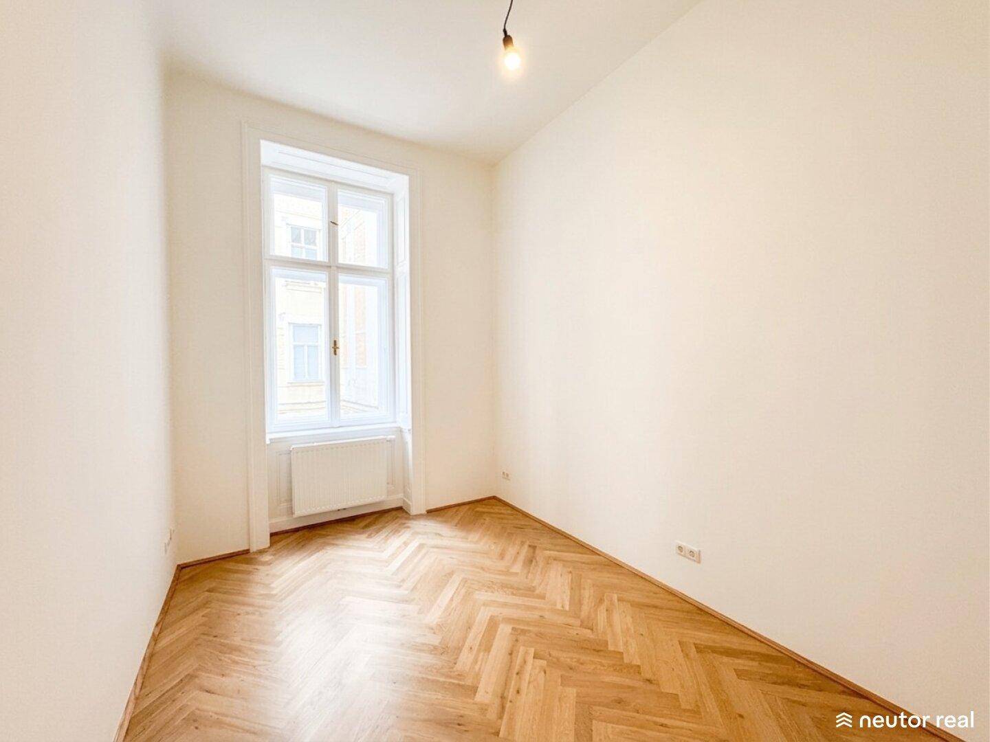 Kleineres, helles Zimmer mit Fischgrätparkett und großem Fenster, ideal als Arbeitszimmer.